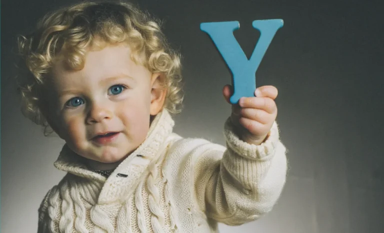 A curly-haired toddler in a cozy sweater holds up a blue letter "Y."