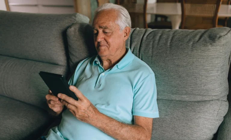 an old man sitting on a sofa using tablet
