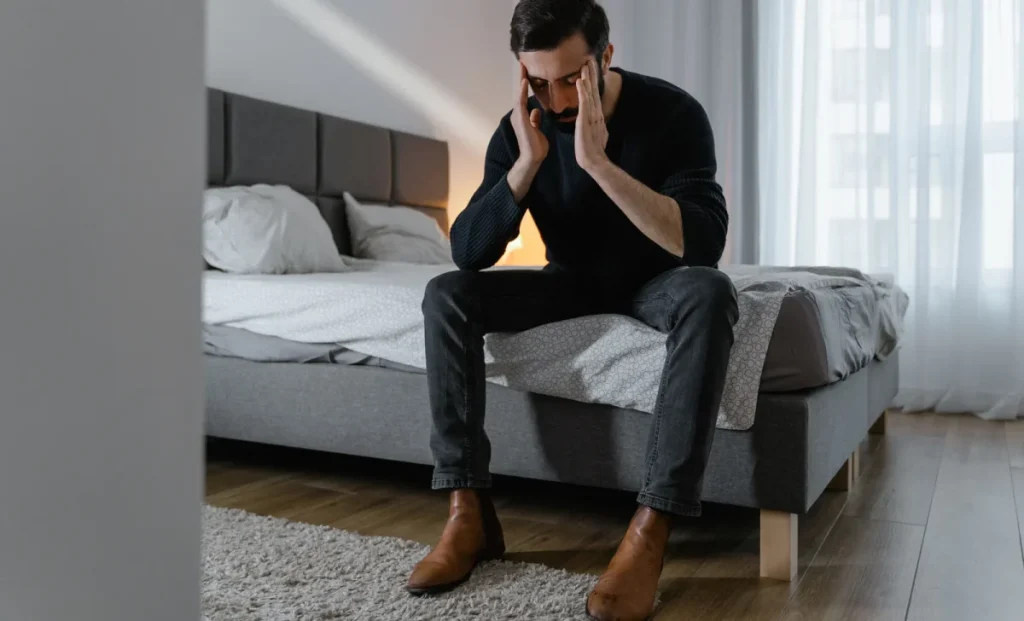 Man sitting on the edge of a bed with his head in his hands