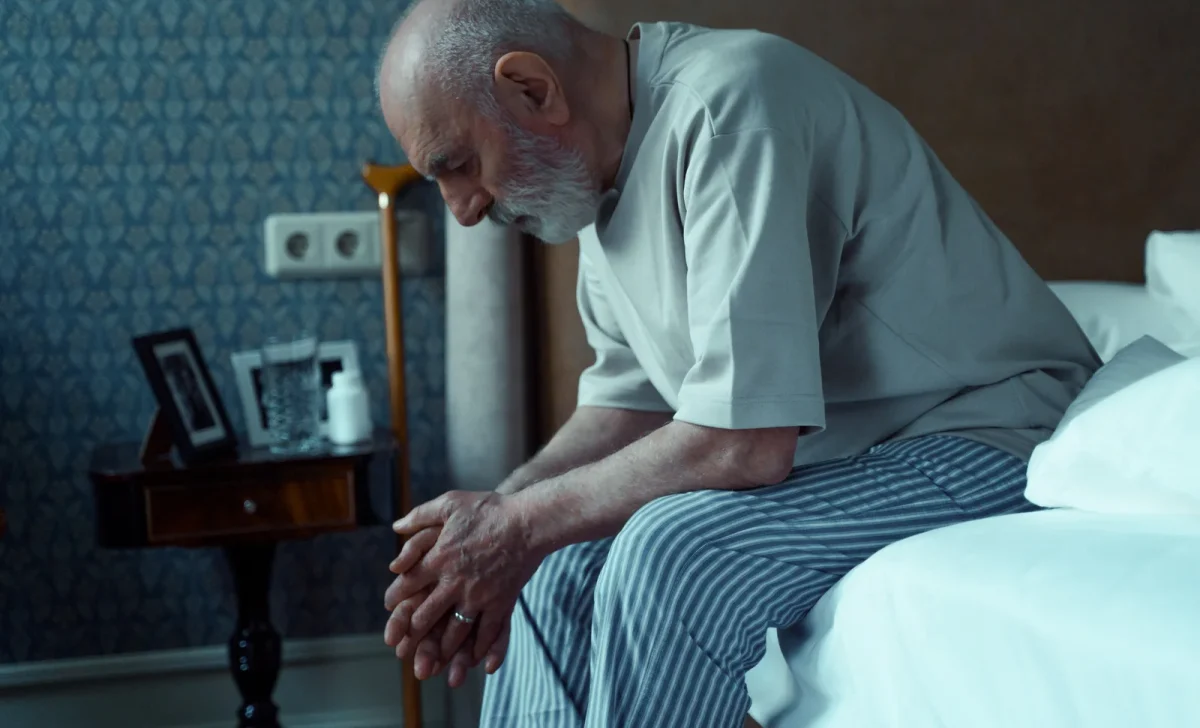 sad old man sitting on a bed