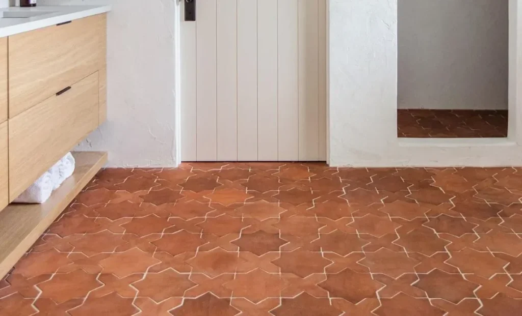 Terracotta star-pattern tile floor in a rustic white-walled interior with a wooden vanity