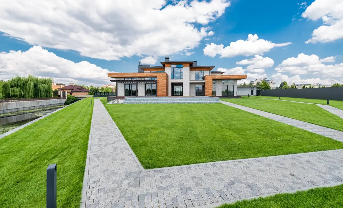 Modern house with manicured lawn, paved walkways and landscaped garden under a blue sky