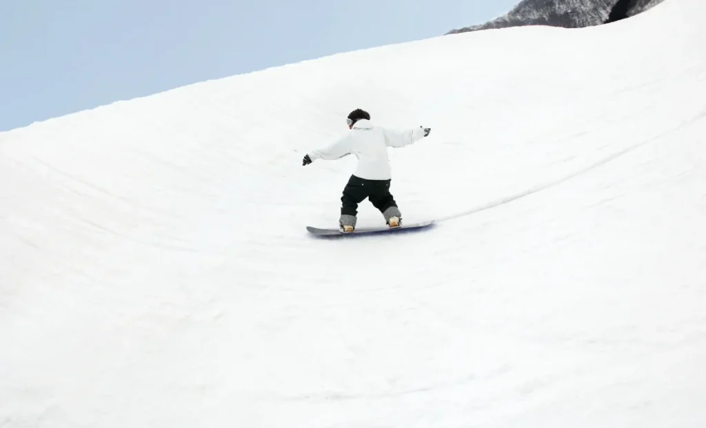 Snowboarder in a white jacket riding down a wide snowy slope